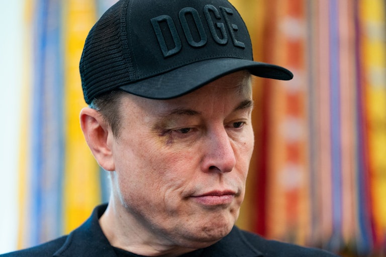 Elon Musk looks down while standing in the Oval Office